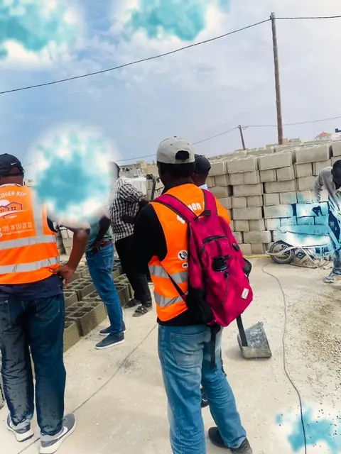Équipe en gilets orange devant des parpaings sur un chantier
