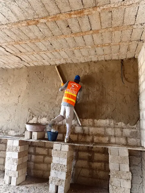 Maçon de dos qui enduit un mur au talochon