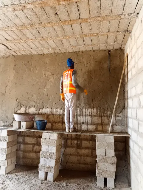 Maçon de dos devant un mur enduit, vue d'ensemble de l'ouvrage